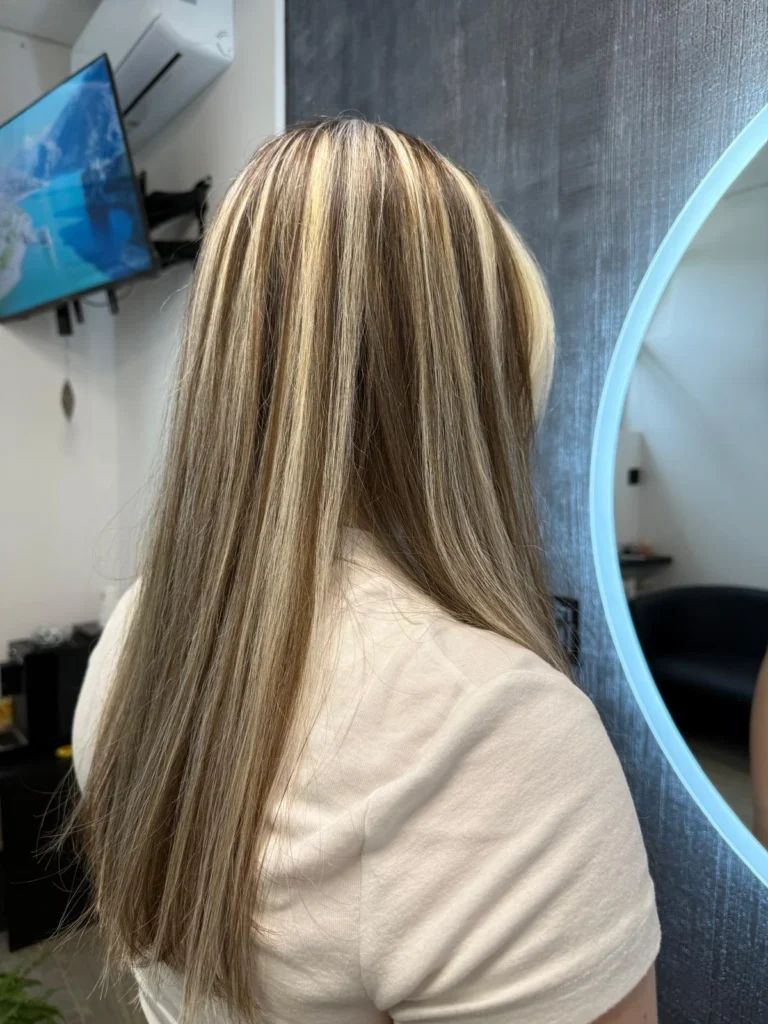 Włosy kobiety po profesjonalnej koloryzacji w odcieniach blondu i jasnego brązu, lśniące i idealnie wygładzone.